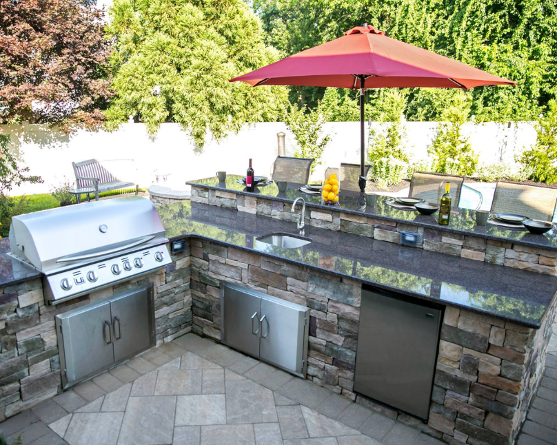 Outdoor backyard patio with built-in stone grill, counter seating, and a red umbrella under trees
