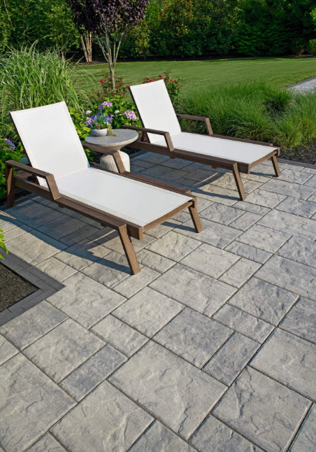 Two white lounge chairs with side table on a stone patio beside a green garden