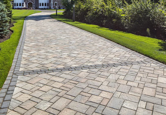 Stone driveway leading to a house, bordered by green lawn and shrubs.