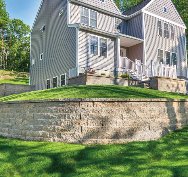 Gray two-story house on a stone retaining wall with a small front porch and green lawn