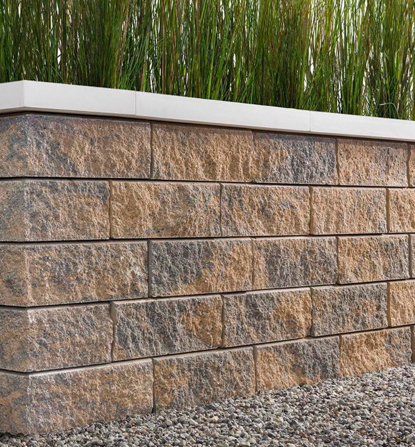 Stone retaining wall with tan blocks, white cap, and tall green grasses behind it.