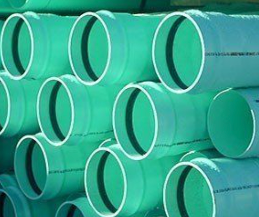 Stacked green plastic pipes with white rims arranged in rows