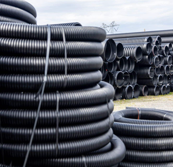 Stacks of black corrugated plastic pipes stored outdoors at a construction site