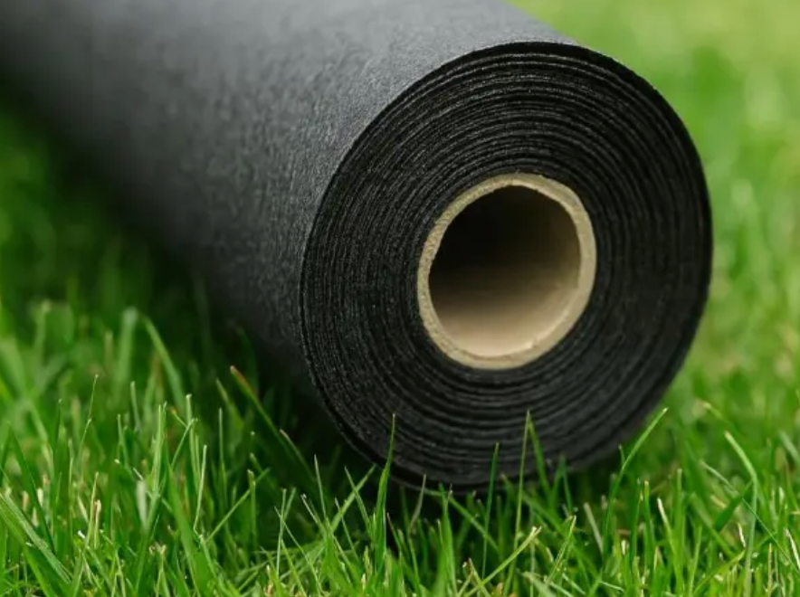 Rolled black turf mat on green grass with a cardboard core