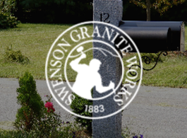 White Seneca Granite Works logo on a gray post beside a mailbox and road in a grassy area