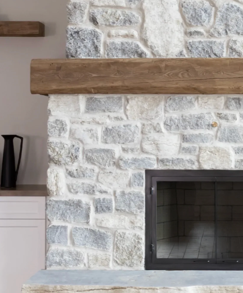 White stone fireplace with a thick wooden mantel and dark metal firebox in a modern room