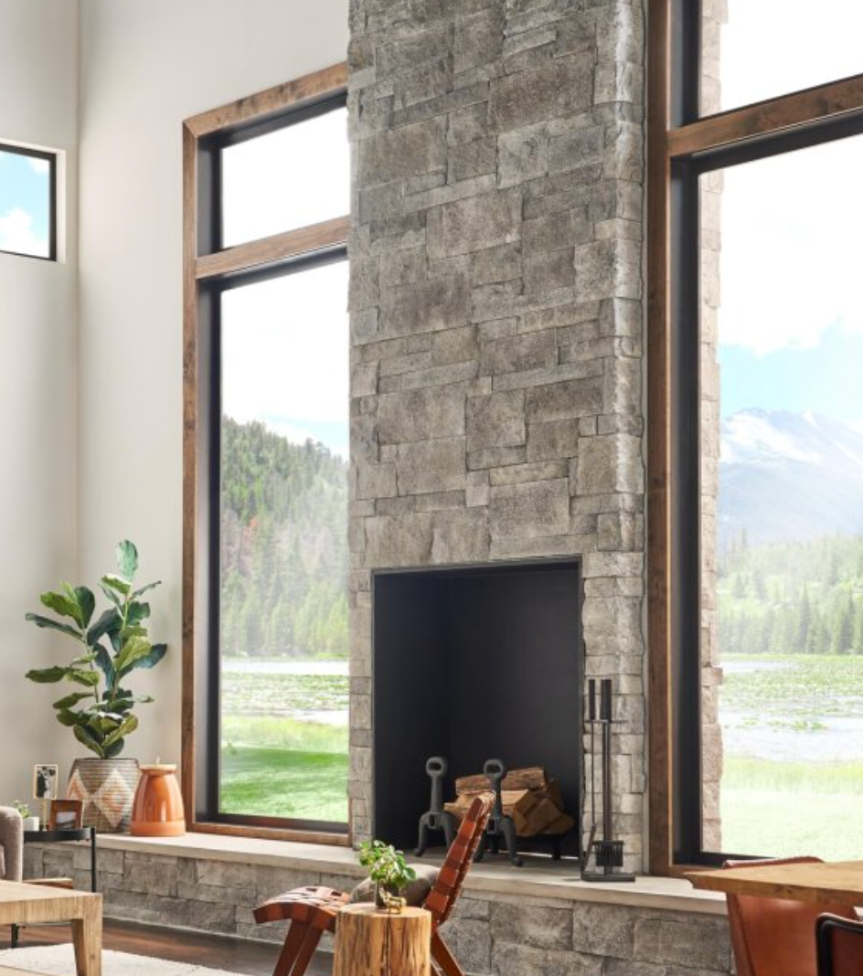 Modern living room with a tall stone fireplace and large windows overlooking mountains and trees