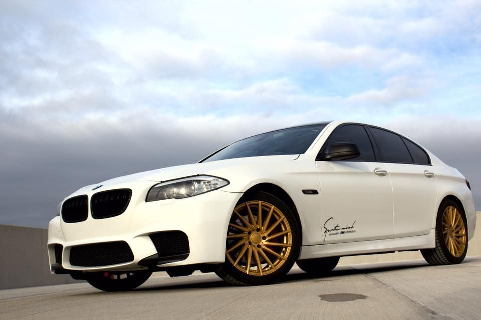 a white bmw with gold wheels is parked on the side of the road