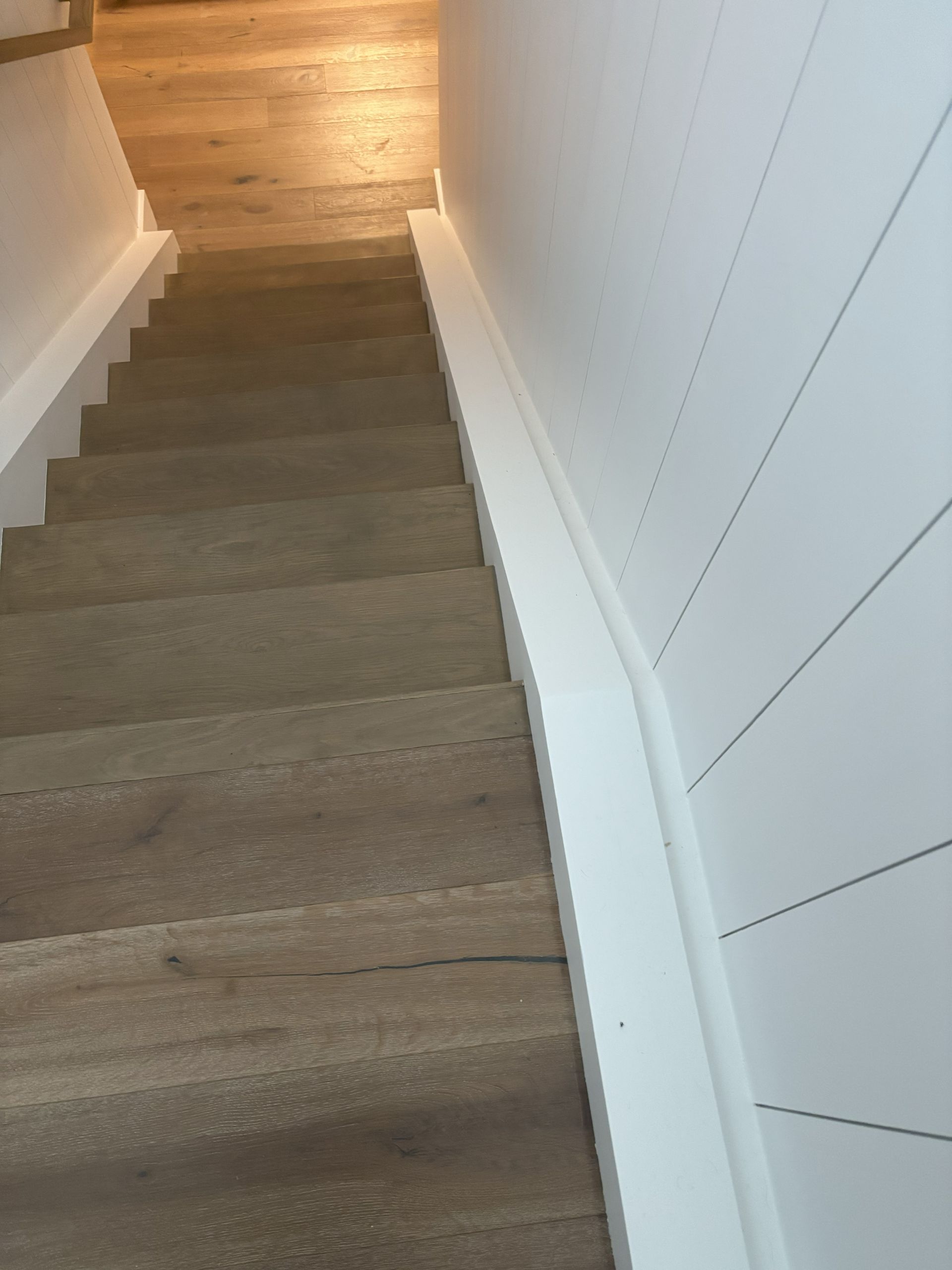 Staircase with gray steps and white walls, one side with horizontal paneling, leading downward.