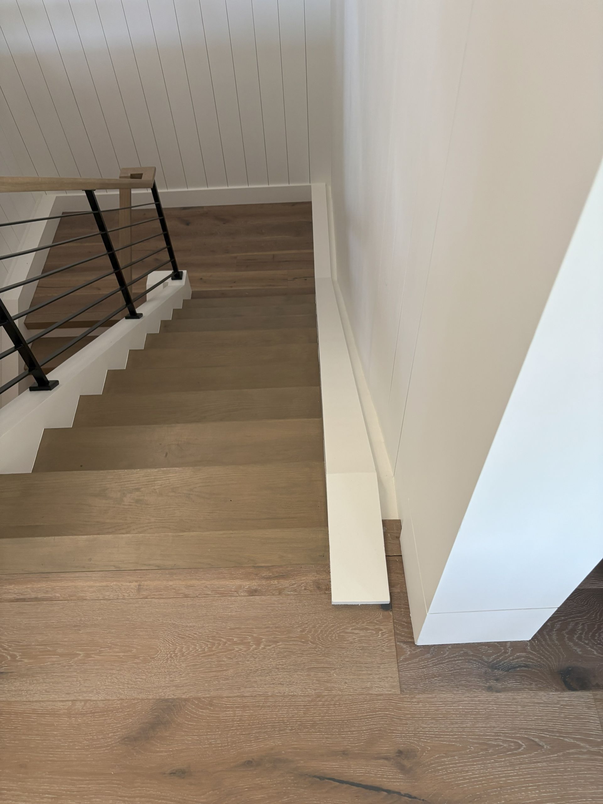 Wooden staircase with a black railing and white wall.