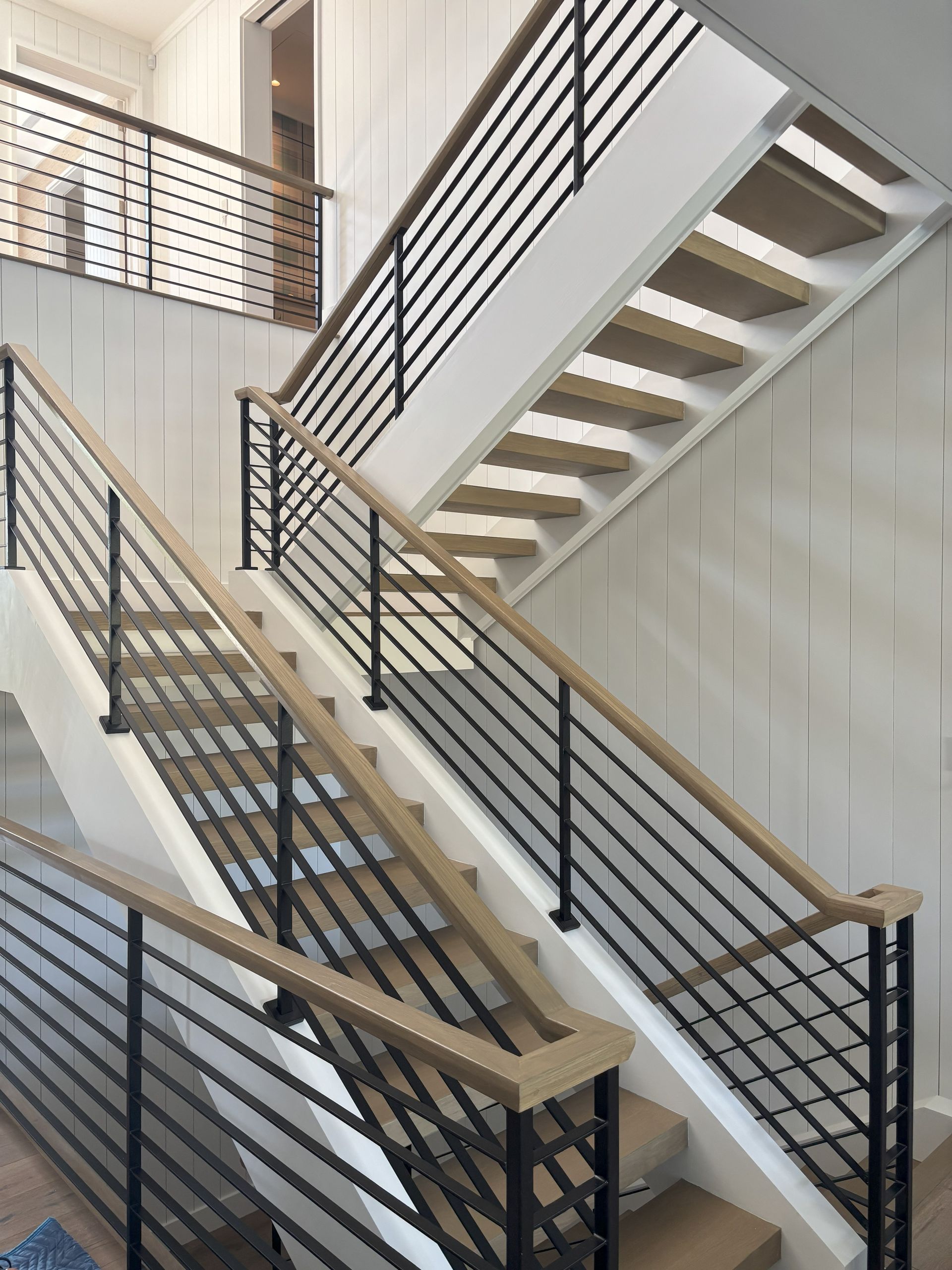 Staircase with wooden steps and black metal railings; white walls.