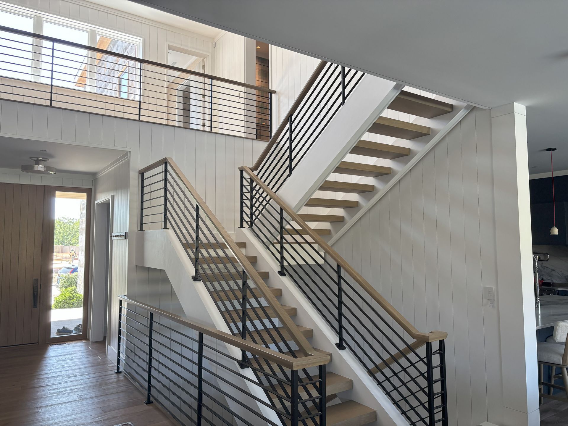 Modern staircase with black metal railings and light wood steps, open to a second floor.