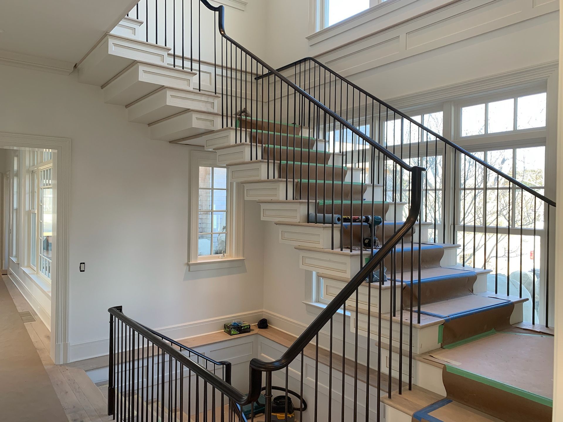 Staircase with black railing and white steps. Windows on the right. Wooden floors.