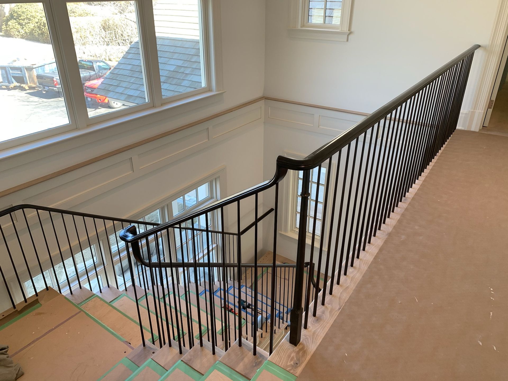 Black iron railing on a stairwell with windows, light walls, and exposed green tape on steps.