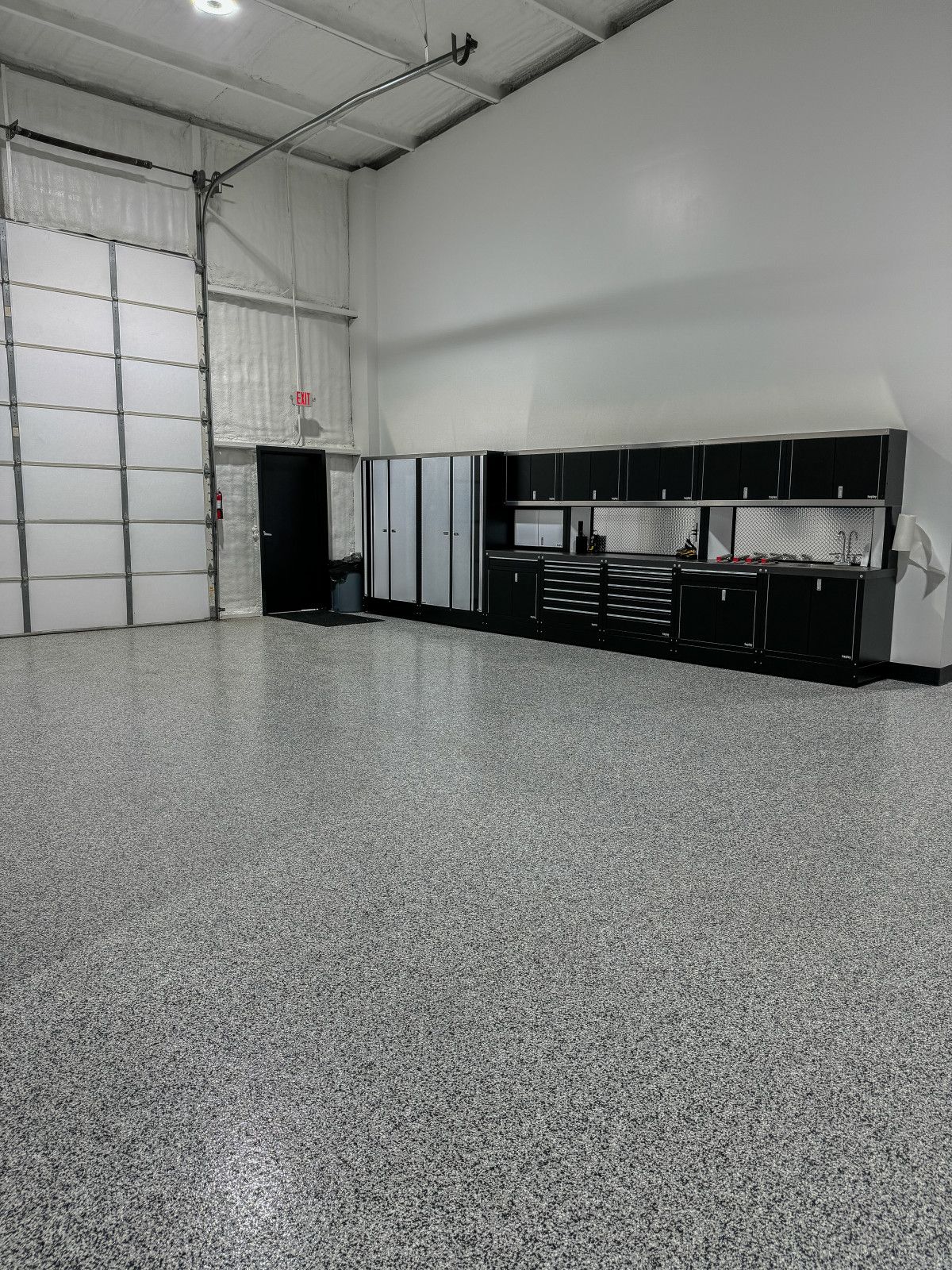 A garage with a gray floor and black cabinets and a garage door.