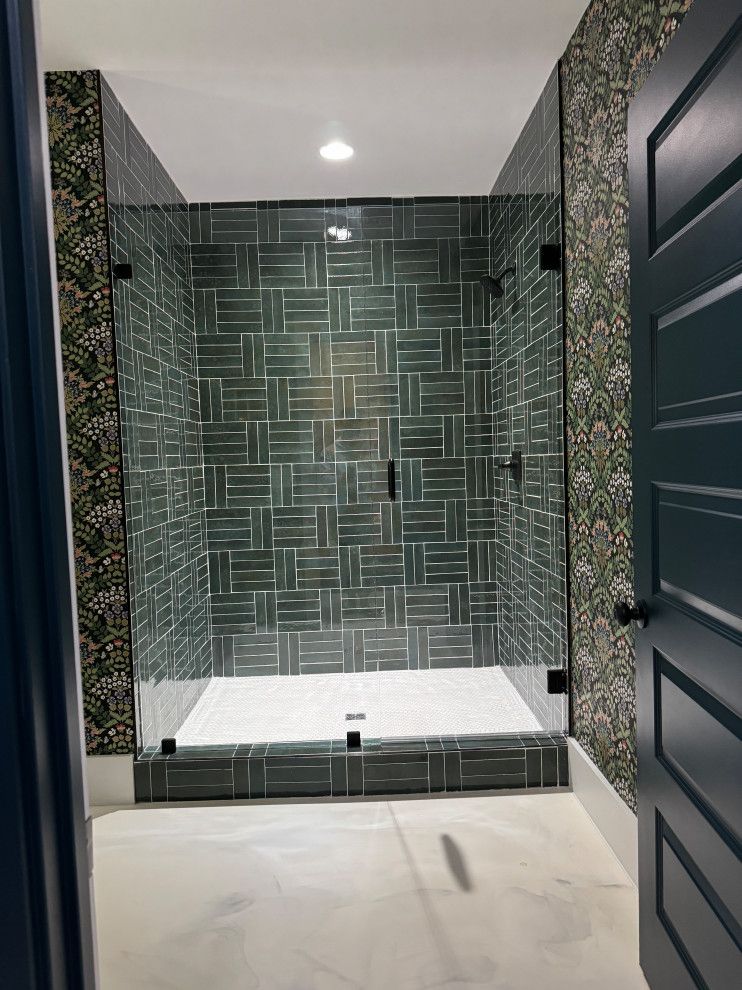 A bathroom with green tiles and a walk in shower with a glass door.
