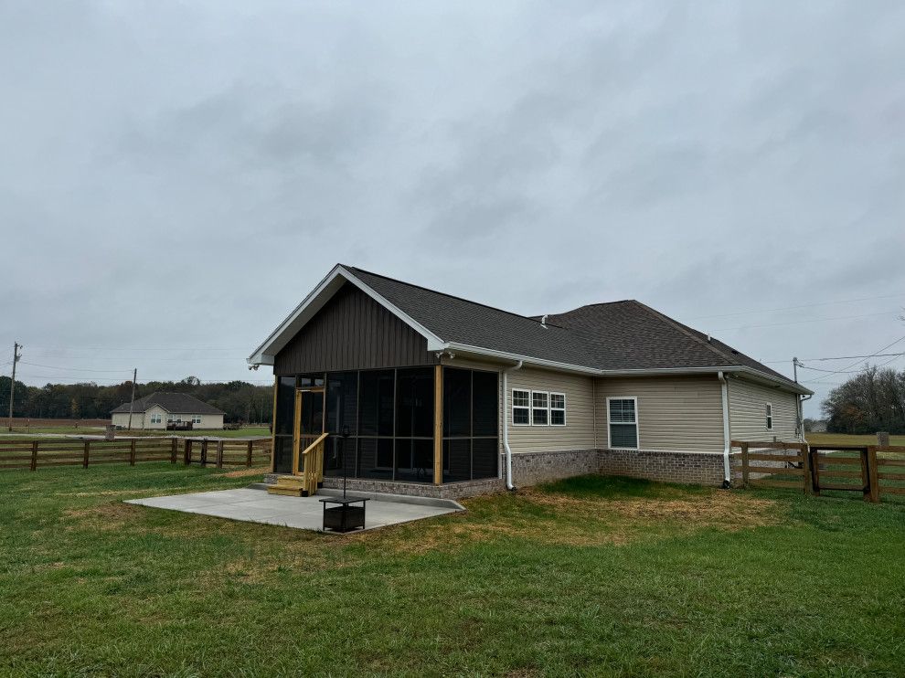 A house with a screened in porch is sitting in the middle of a grassy field.