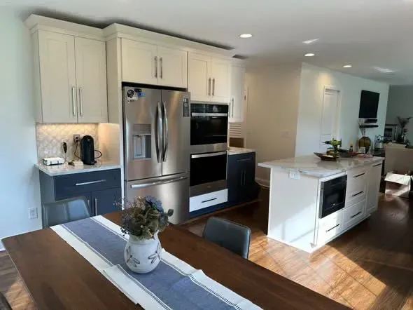 Modern kitchen with white cabinets, stainless steel appliances, a dark blue accent, and a wood dining table.