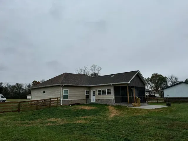 A view of a single-story house on a cloudy day with a screened porch and fenced backyard.
