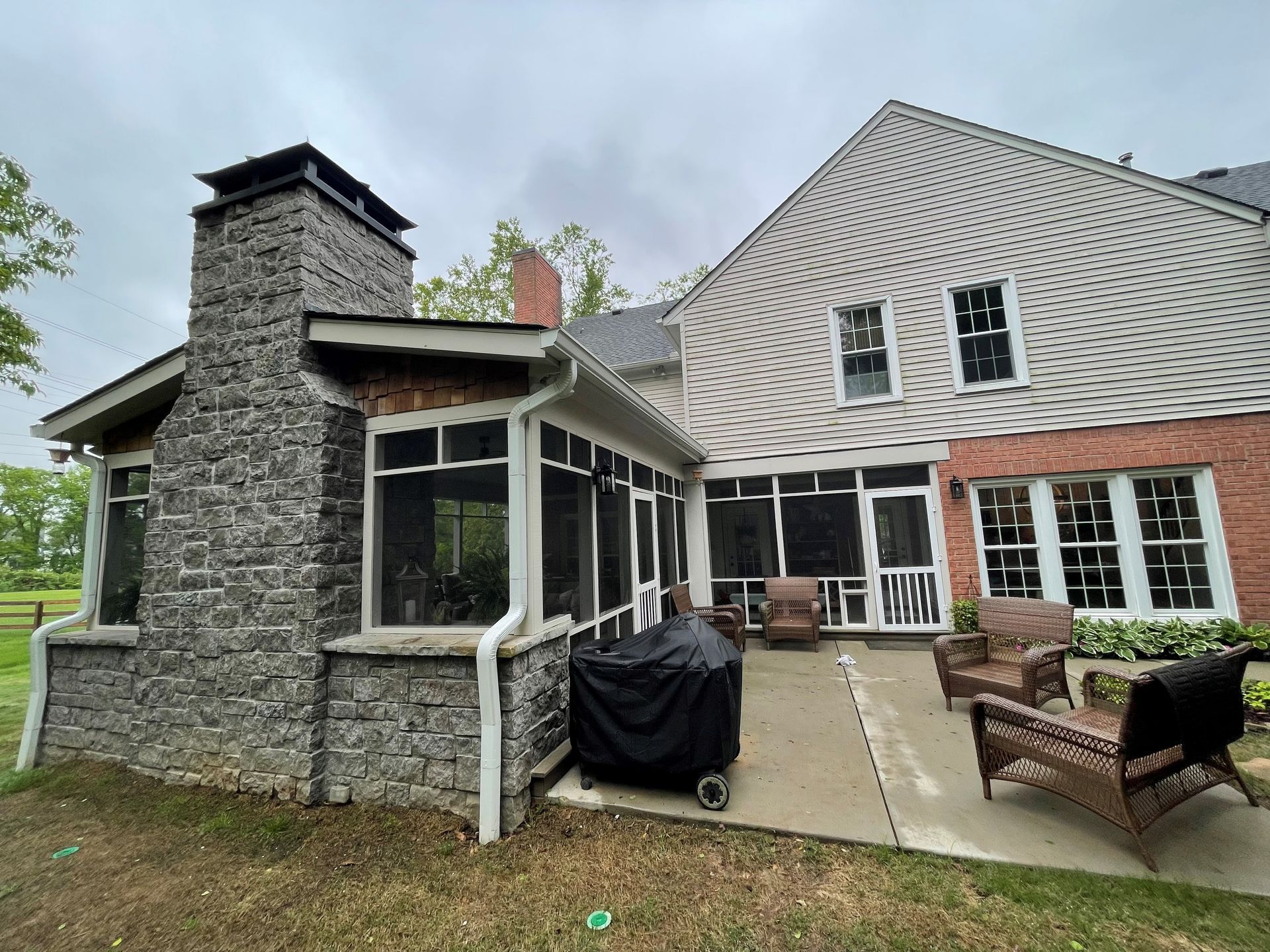 The back of a house with a screened in porch and a fireplace.