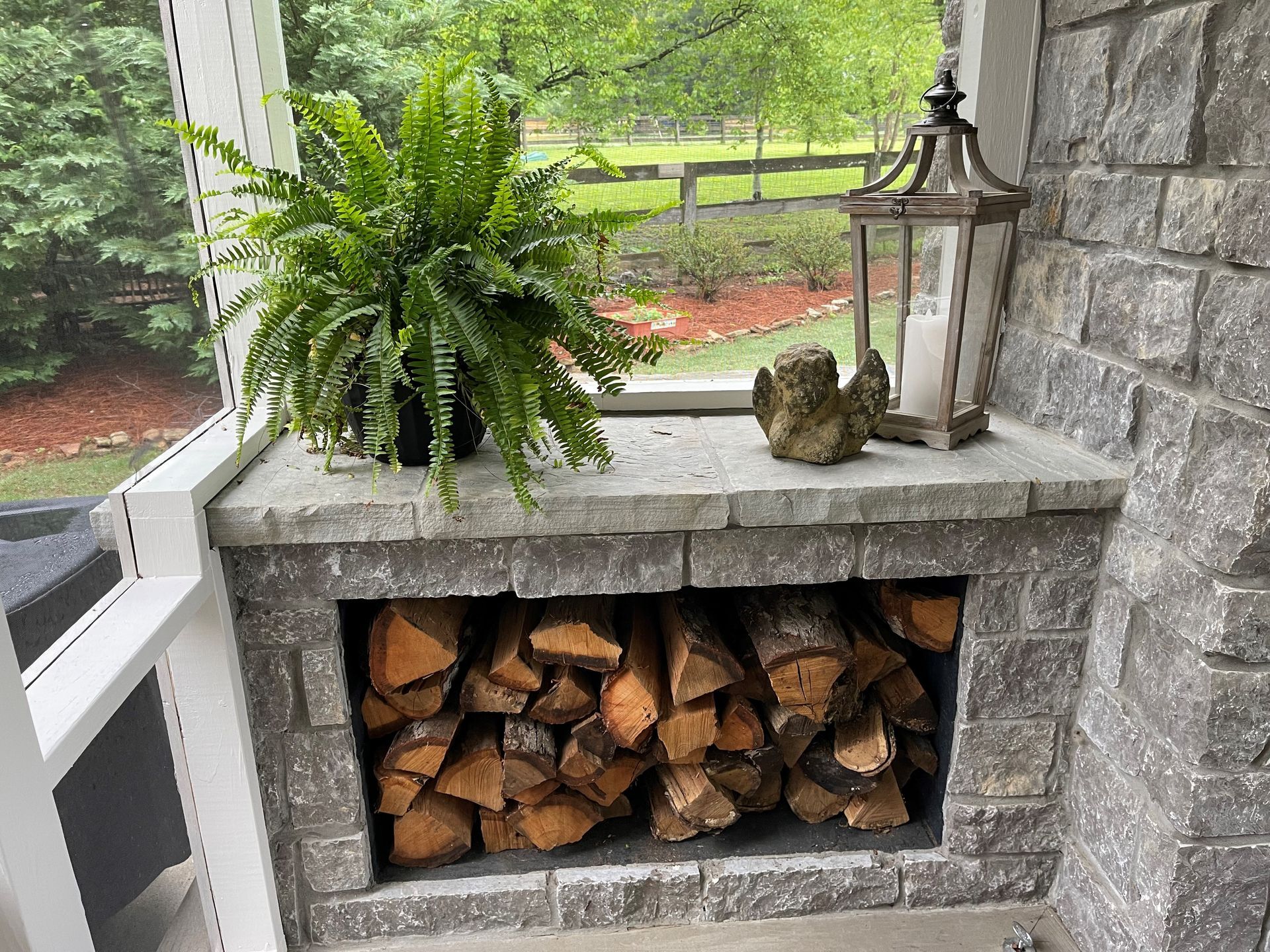 A fireplace filled with logs and a plant on a porch.