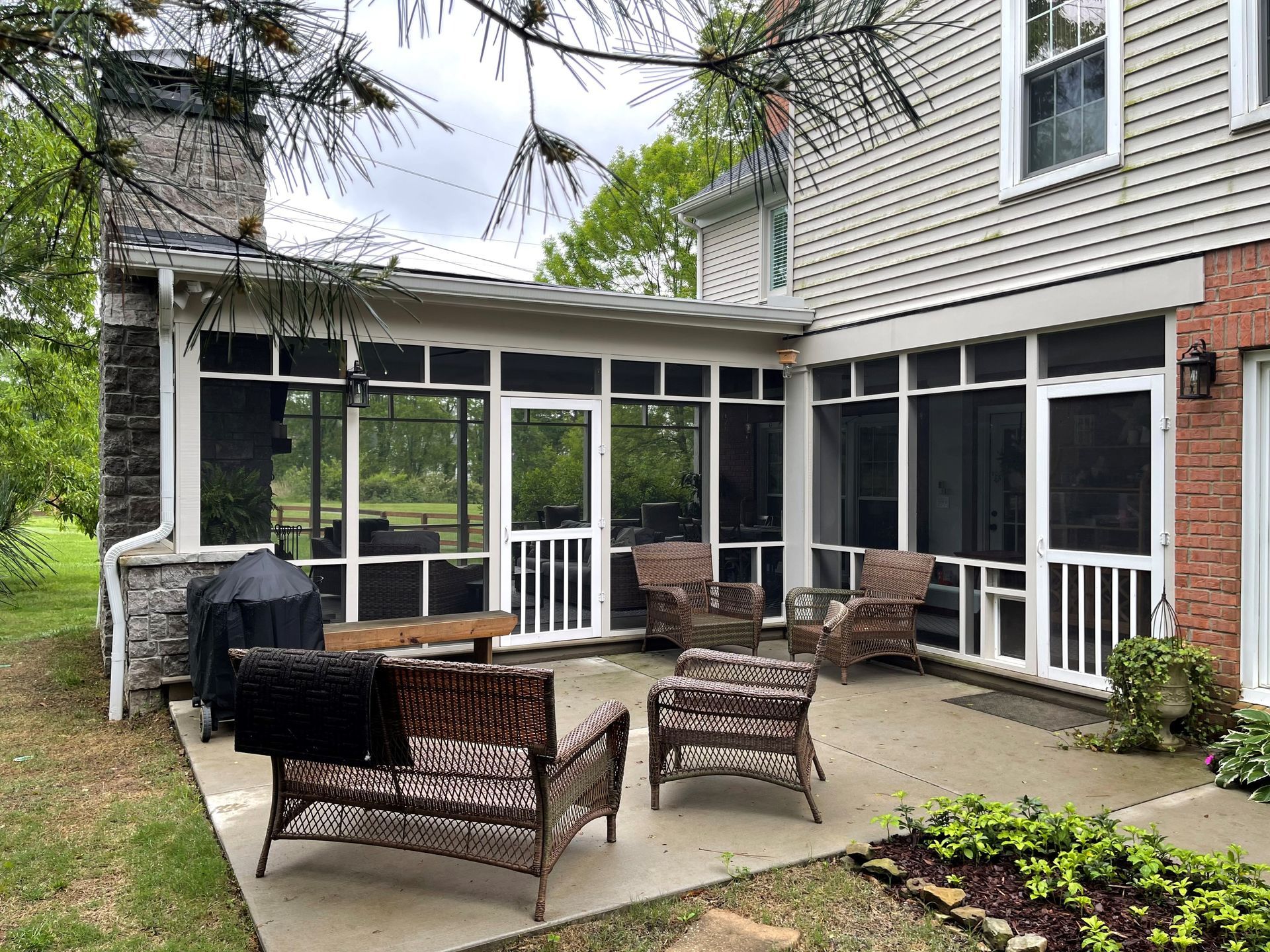 A screened in porch with wicker furniture and a grill.