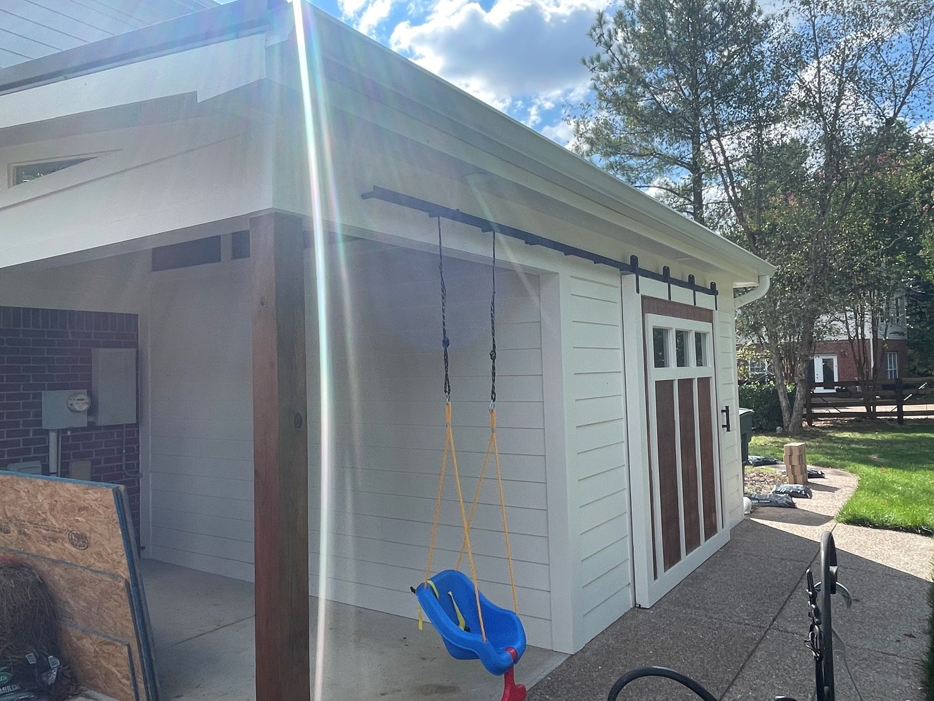 A blue swing is hanging from the side of a white shed.