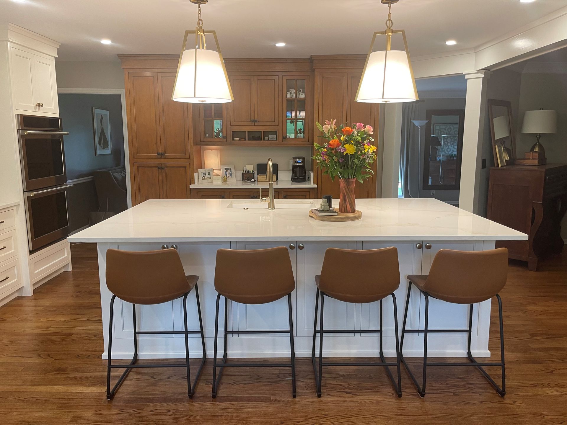 A kitchen with a large island and stools and a vase of flowers on the counter
