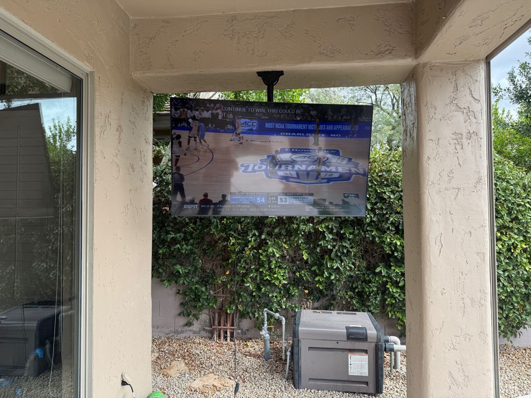 A large flat screen tv is hanging from the ceiling on a patio.