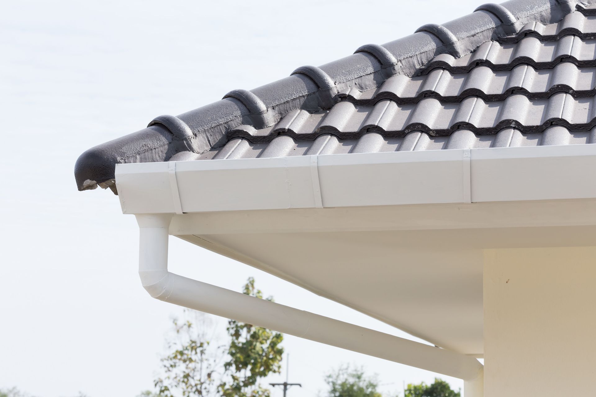 Close-up of a house roof with dark gray tiles, white eaves, and guttering against the sky