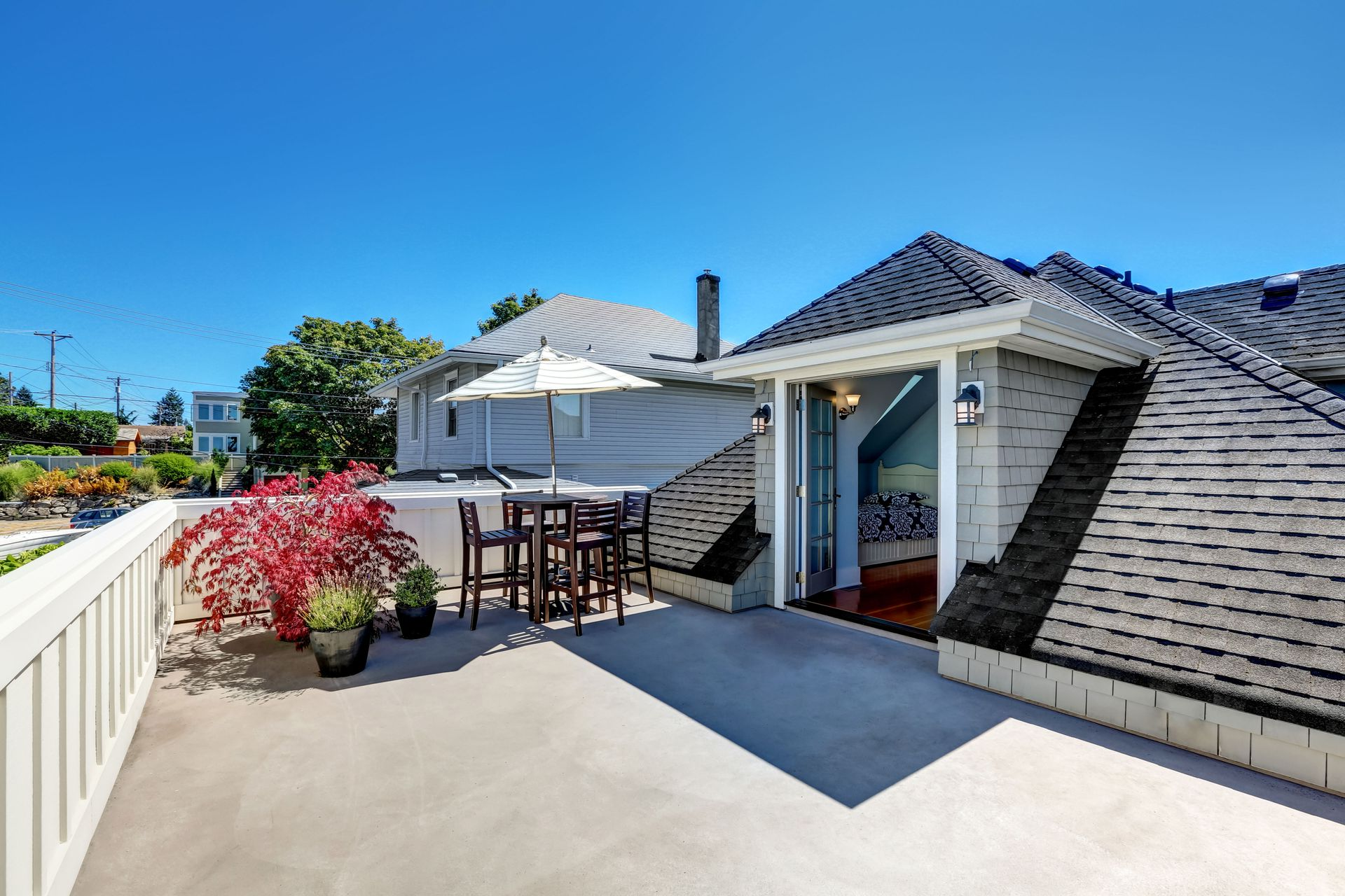 Rooftop patio with table, white umbrella, potted flowers, and open door under a blue sky