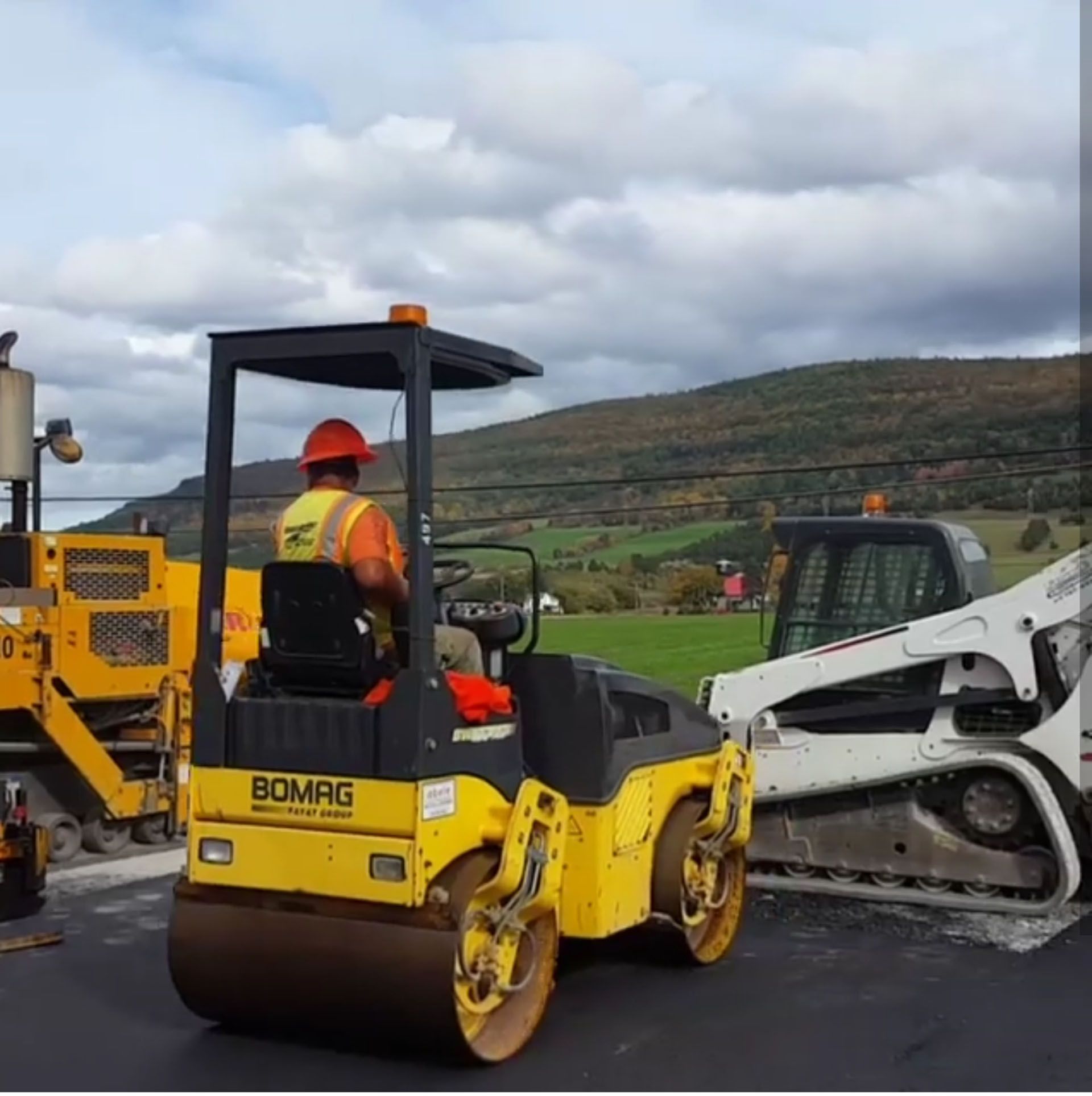 a worker is driving a yellow bomag roller