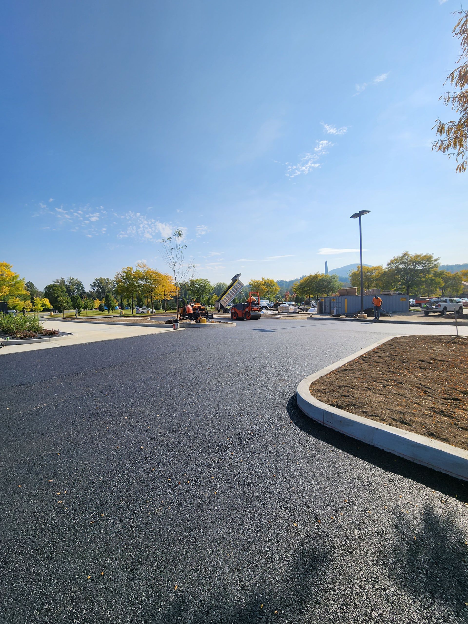 a road is being paved in a parking lot on a sunny day .