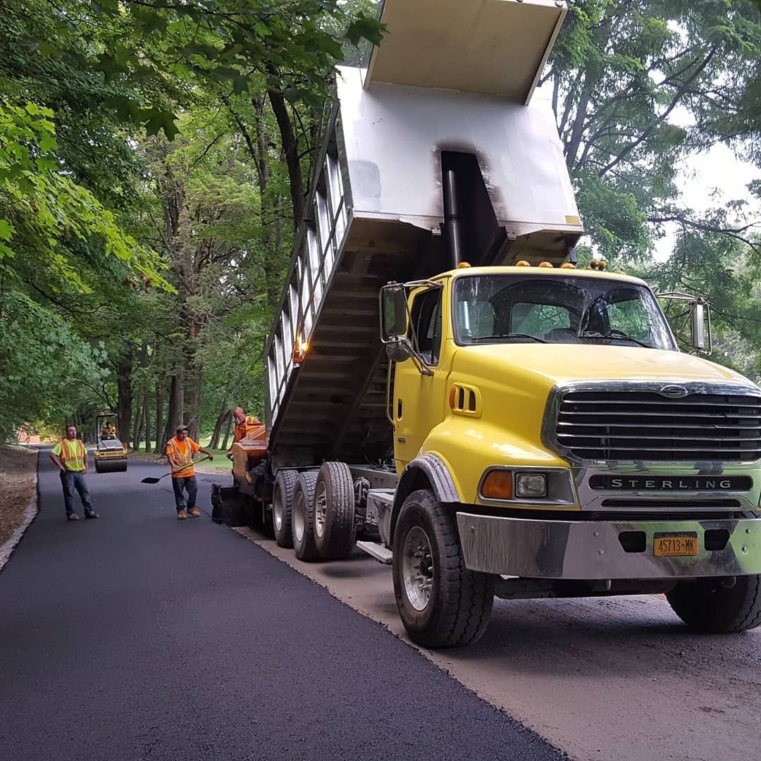 a yellow dump truck is pouring asphalt .