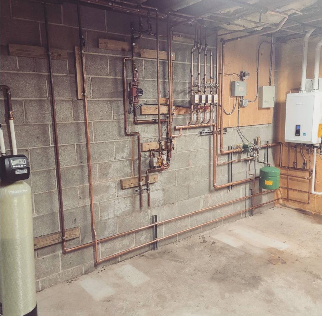 Plumbing pipes and water heater installed in a basement, with a water softener on the left.