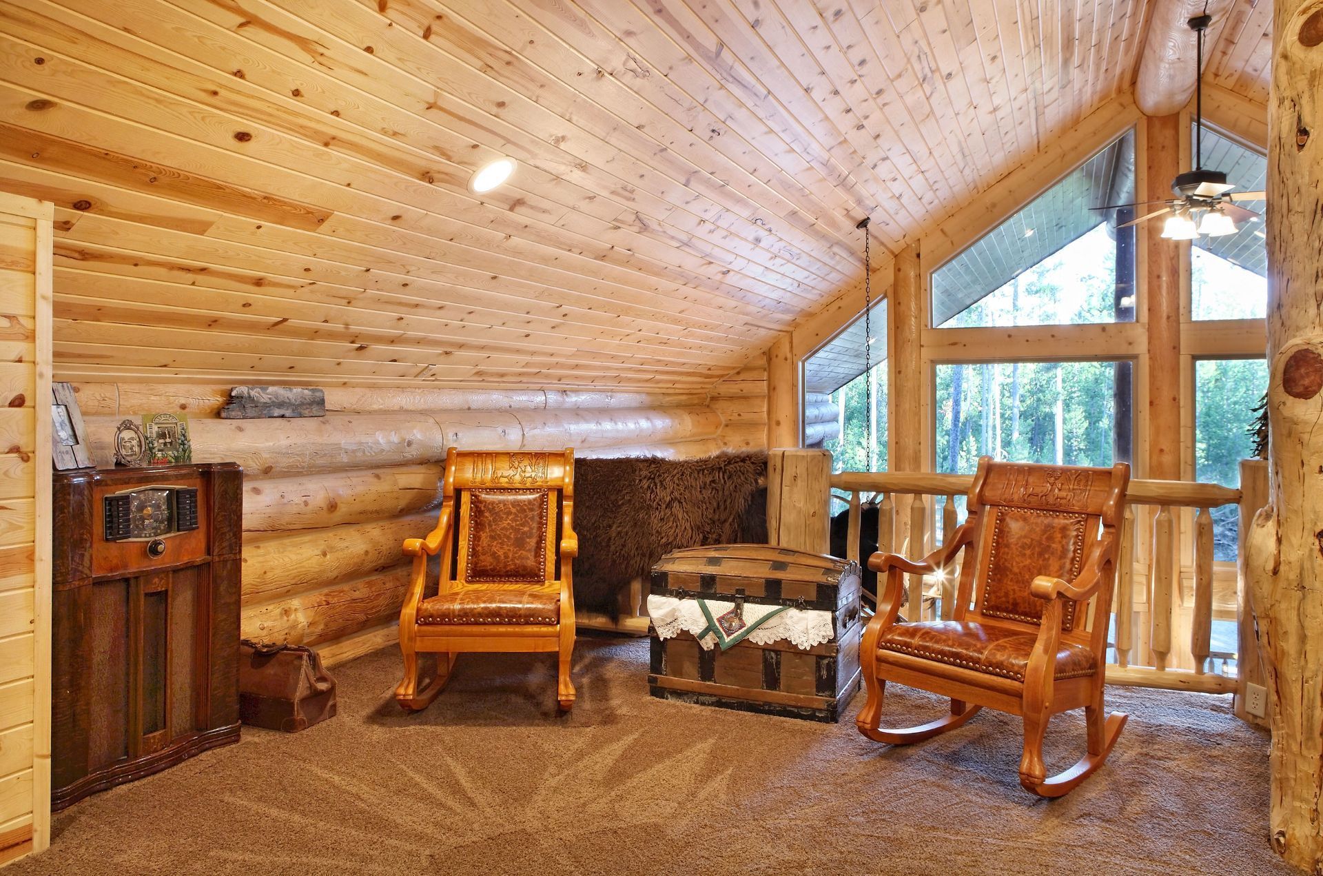 Cozy log cabin living room with rocking chairs, wood-paneled walls, and large windows