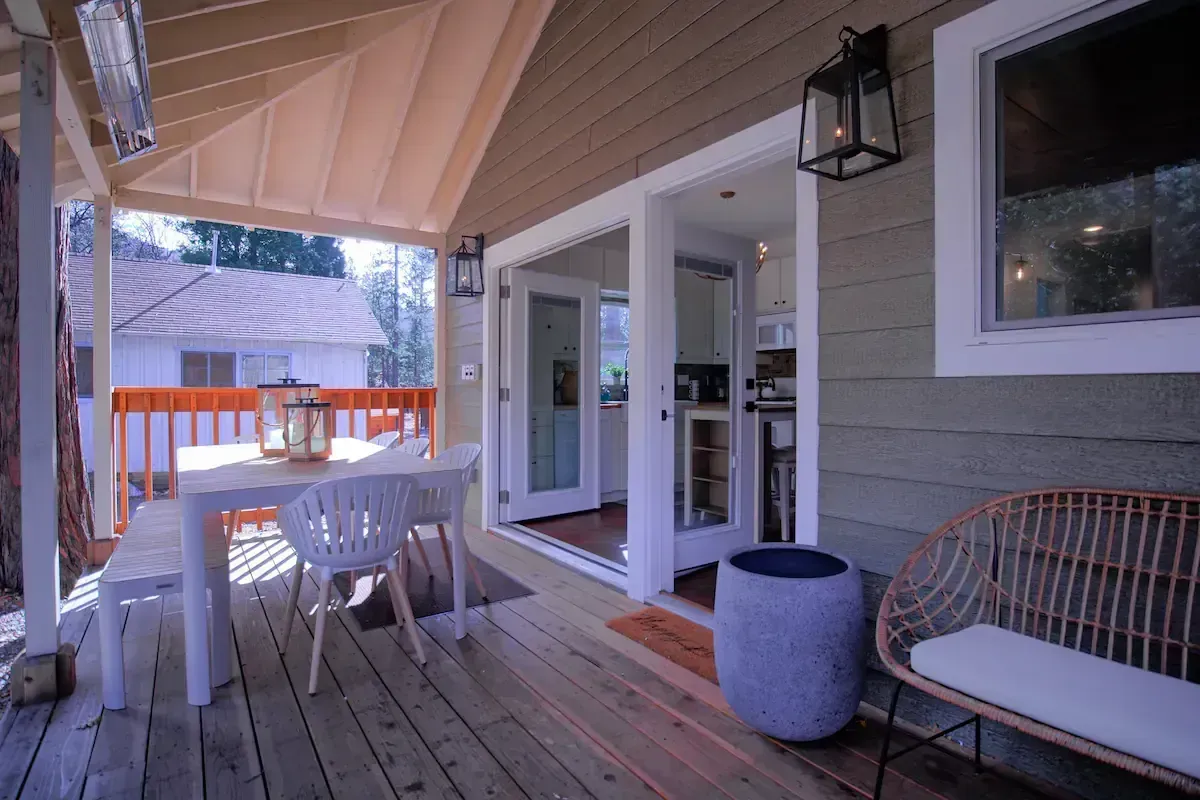 Covered patio with white table and chairs, bench, and potted stool beside a house exterior.