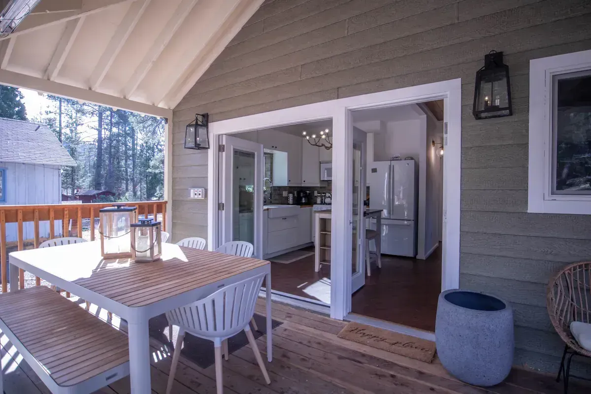 Covered porch with dining table, chairs, and open doors leading into a bright kitchen