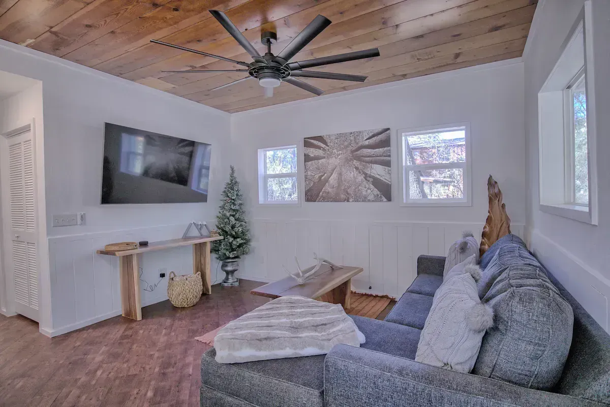 Modern living room with gray sectional, wall-mounted TV, wood ceiling, and large windows