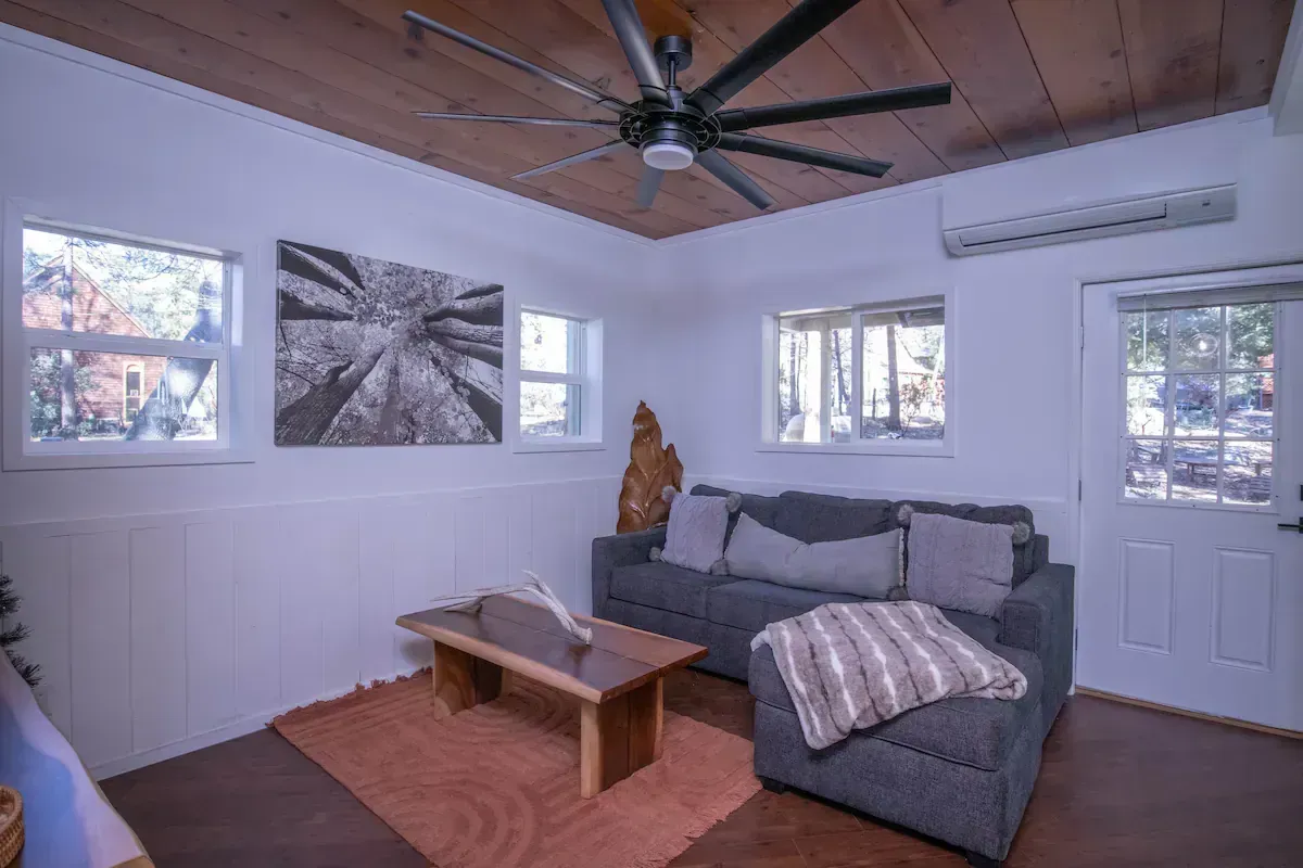 Cozy living room with gray sectional, wood coffee table, ceiling fan, and large windows with a snowy view