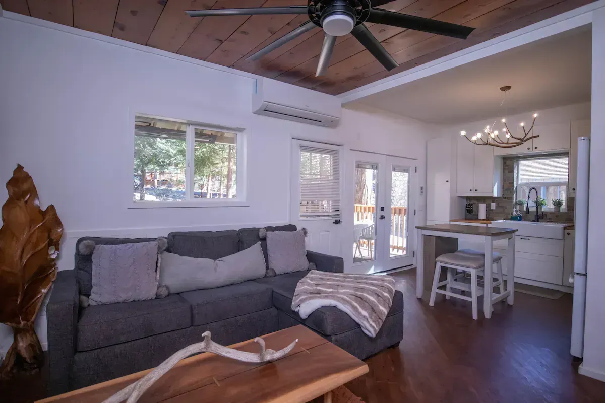 Cozy living room with gray sofa, ceiling fan, wooden floors, and open view into a bright kitchen