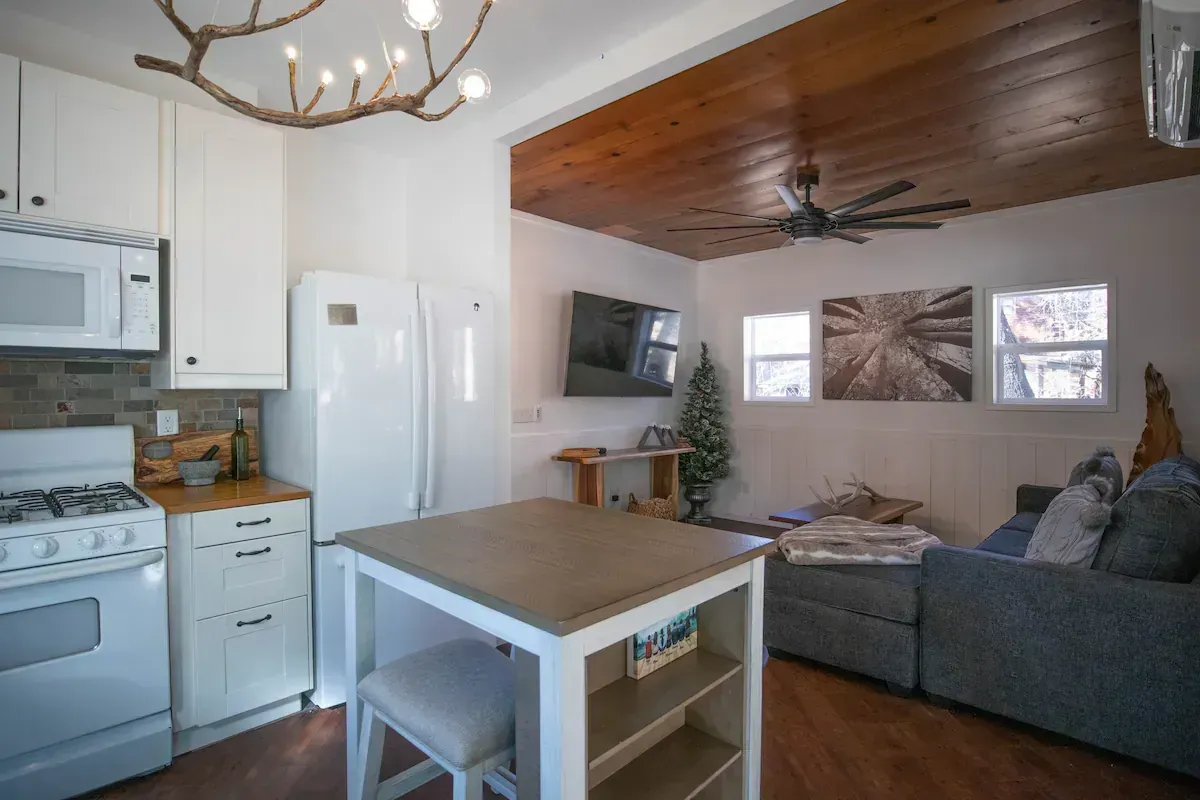 Modern open kitchen and living room with gray sectional, wood ceiling, and white island table