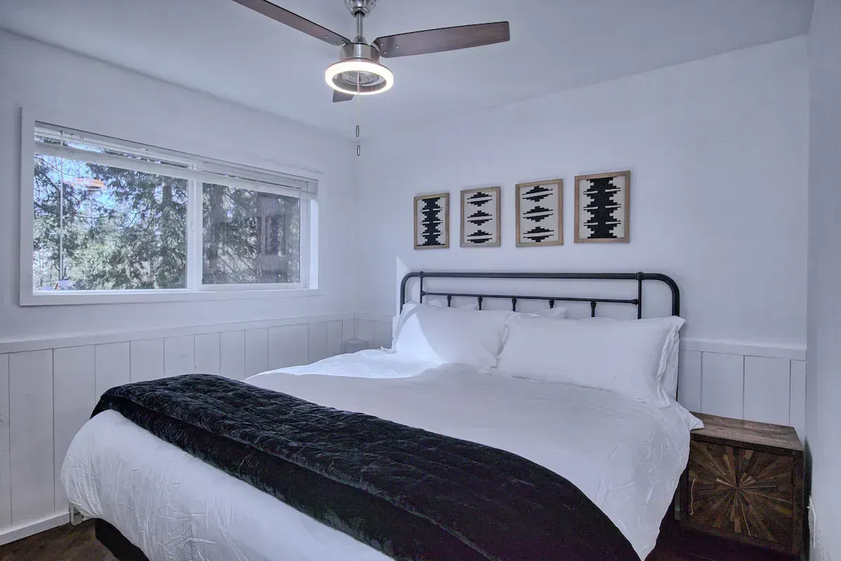 Minimal white bedroom with bed, window, ceiling fan, and framed wall art