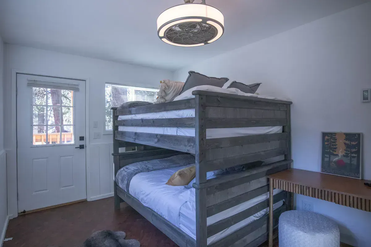 Bedroom with gray bunk bed, white door, window, and desk under a round ceiling light.