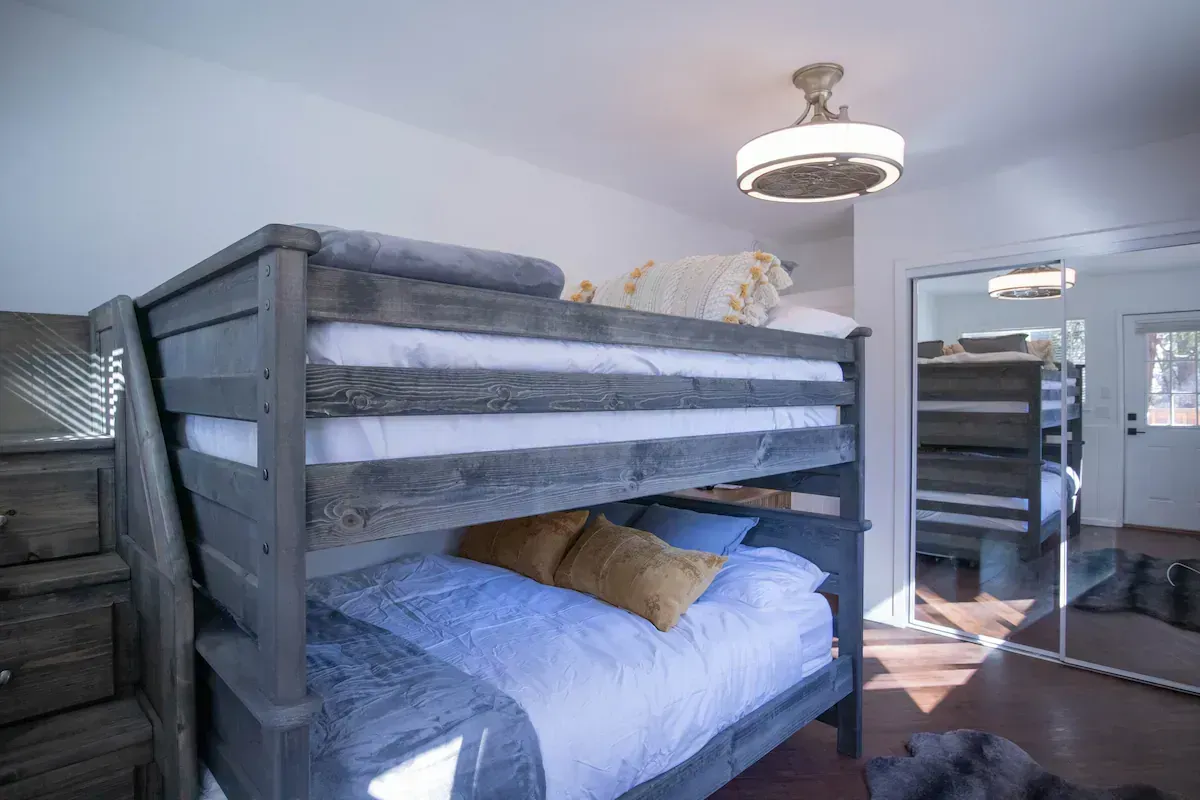 Lofted bunk bed with blue bedding in a bright bedroom, mirrored closet and window in the background