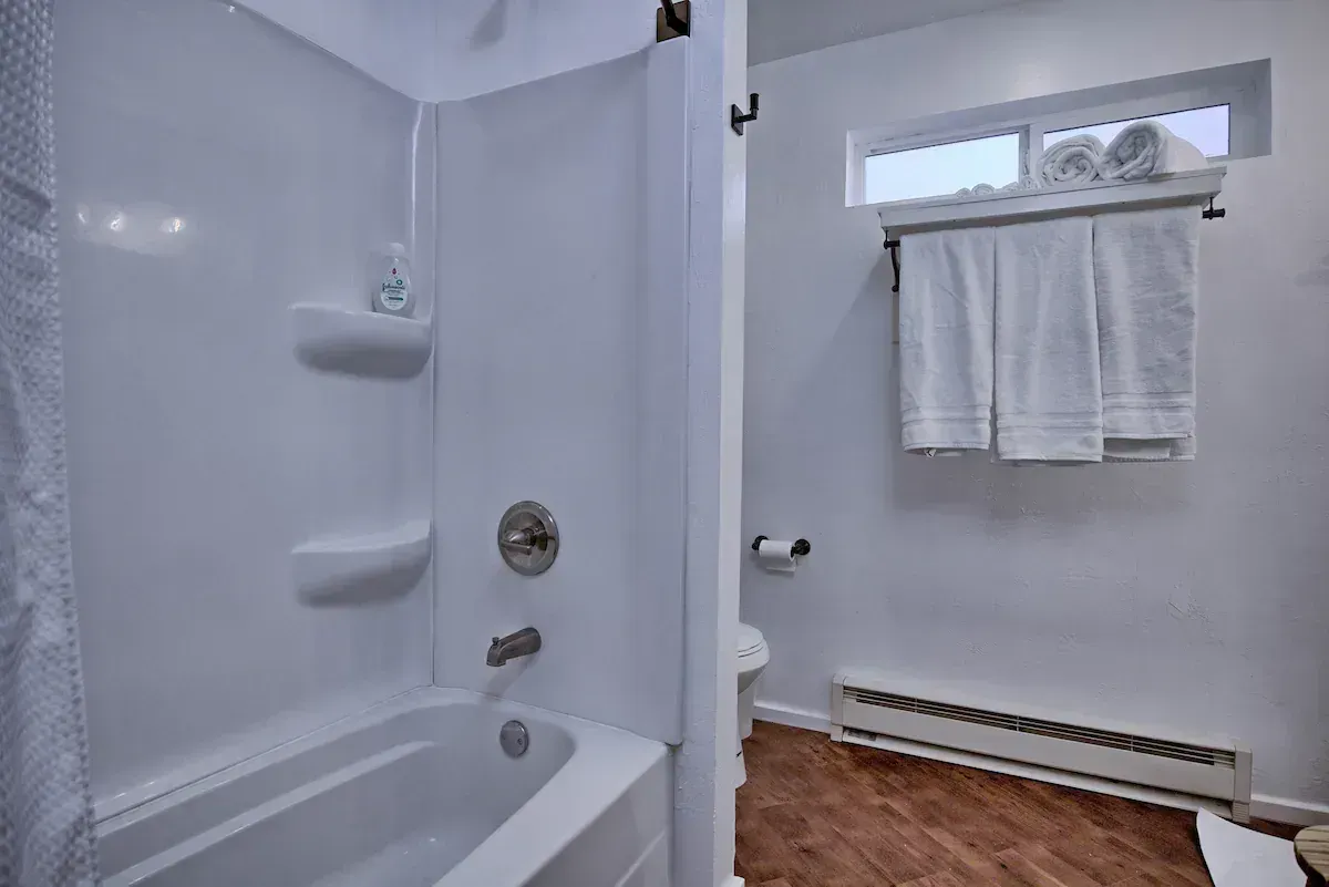 White bathroom with a tub, shower, towel rack, and small window over wood flooring
