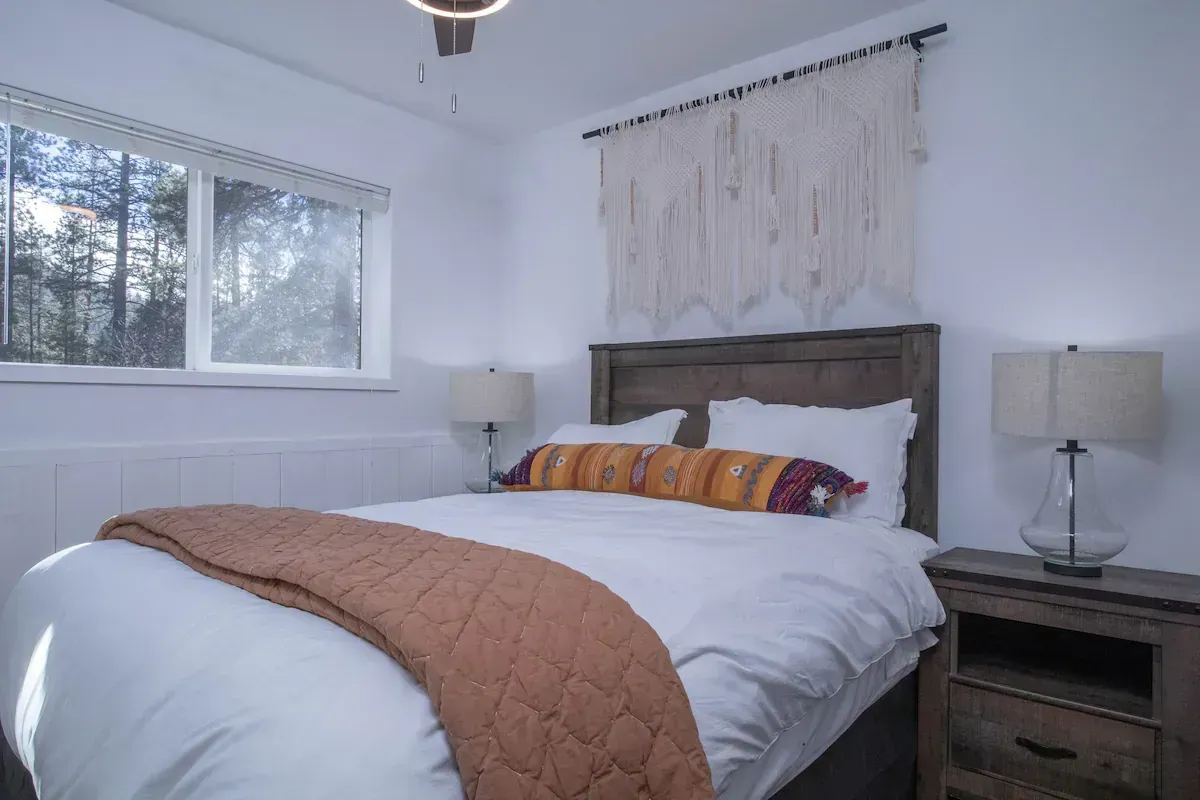 Bright bedroom with white bed, wooden headboard, bedside lamps, and window with blinds