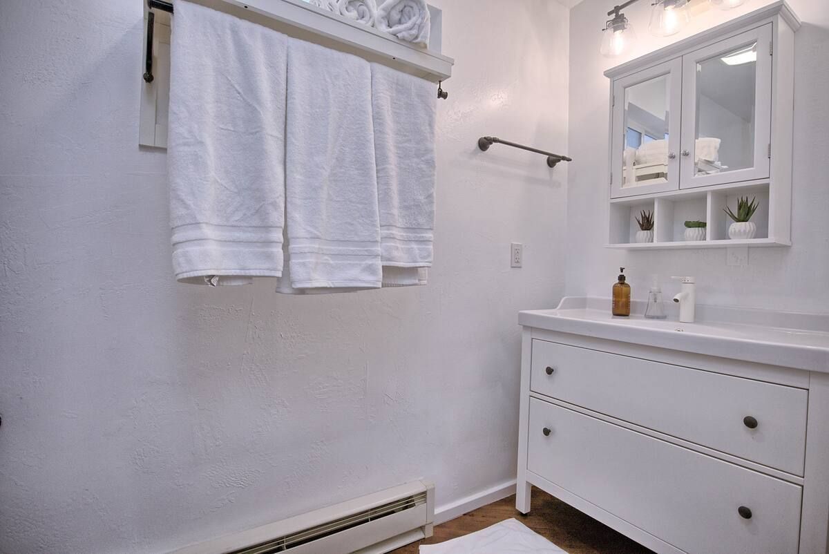 Small white bathroom with towels on a rack, a sink vanity, and a mirror cabinet.