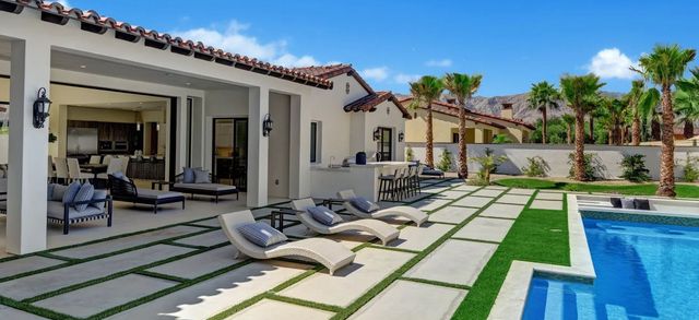 Modern villa patio with lounge chairs, lawn pavers, and a blue swimming pool under a clear sky