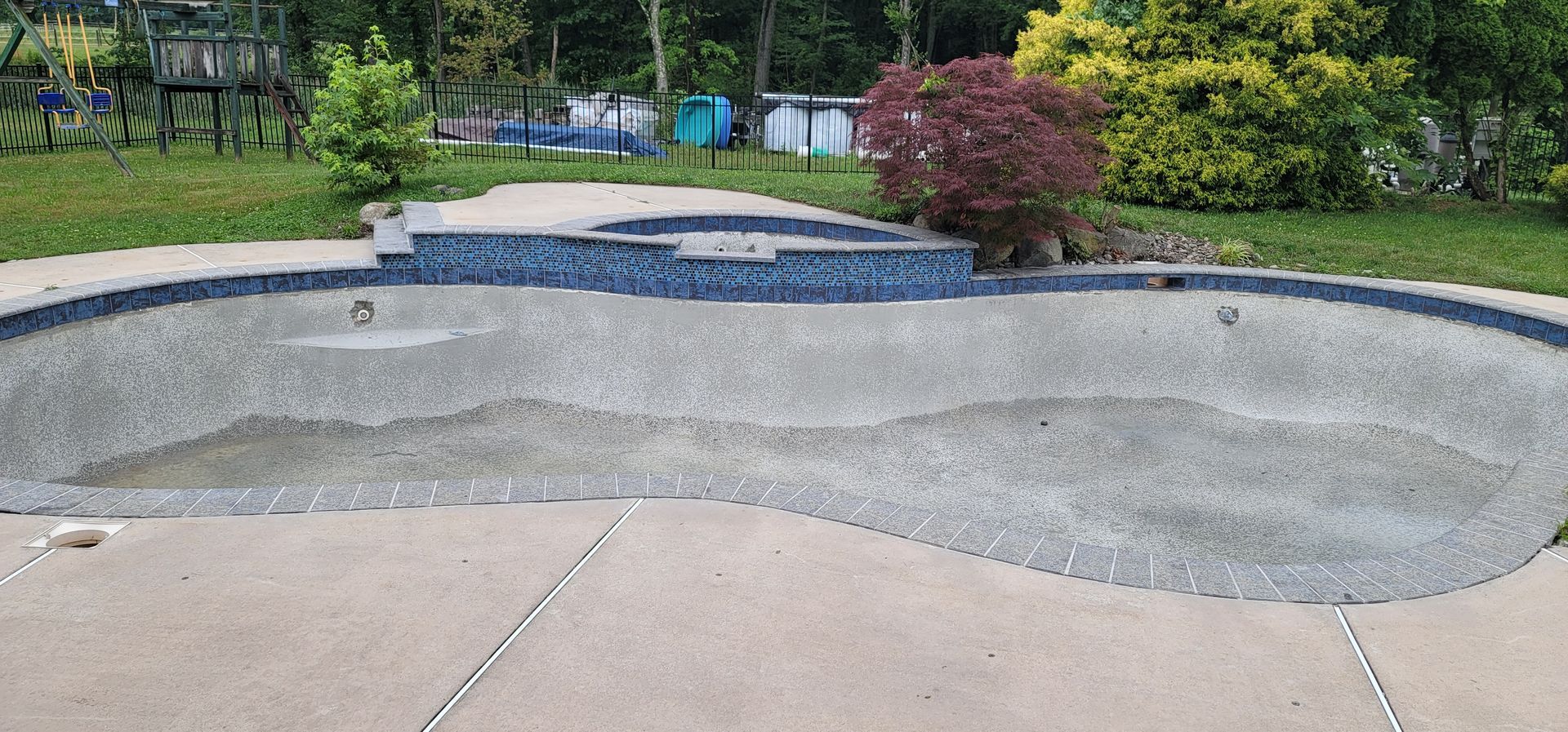 An empty in-ground swimming pool with gray pebble finish and surrounding concrete deck.